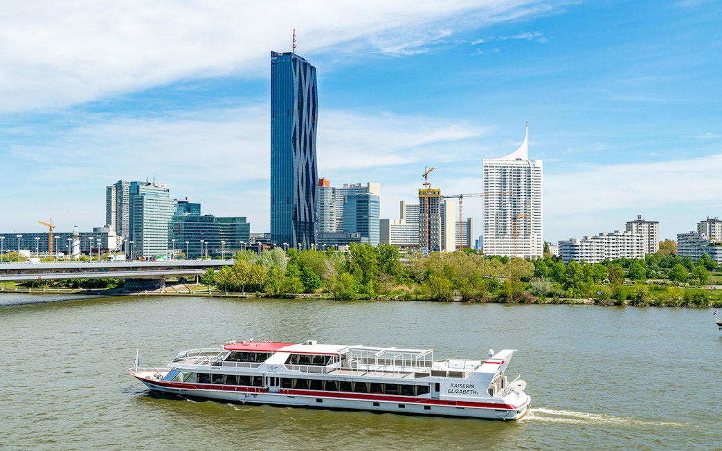 Danube cruise boat on river with Vienna skyline in background.