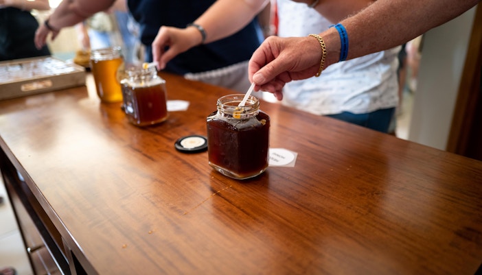 People sampling honey from jars on a wooden table.