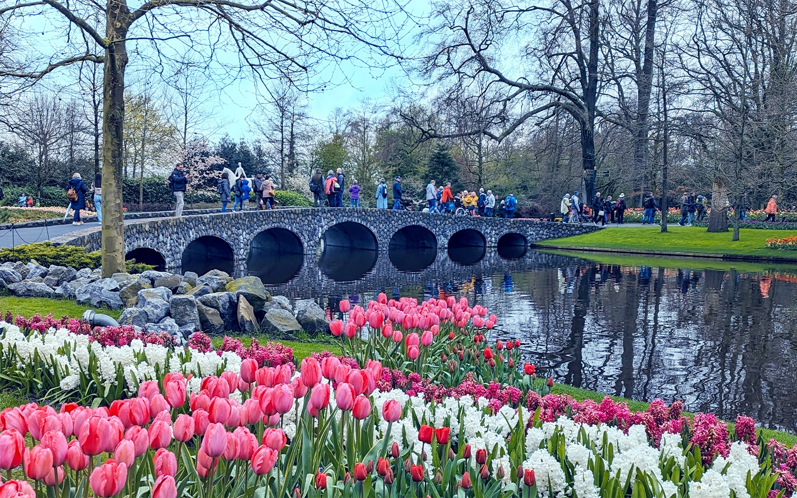 Visitors crossing a stone bridge at Keukenhof Gardens, Amsterdam, with tulips in bloom.