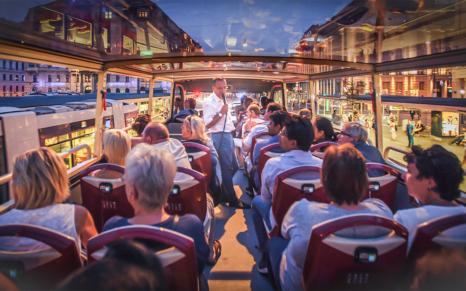 Open-top bus tour in Berlin at night with passengers and guide.