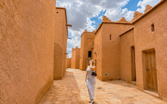 Woman walking through Kasbah Taourirt in Ouarzazate, Morocco under a cloudy sky.