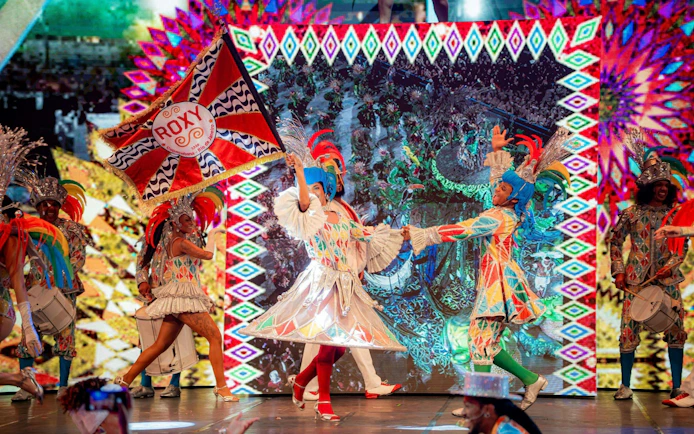 Performers in colorful costumes at Roxy Dinner Show, Rio de Janeiro, holding a vibrant flag.