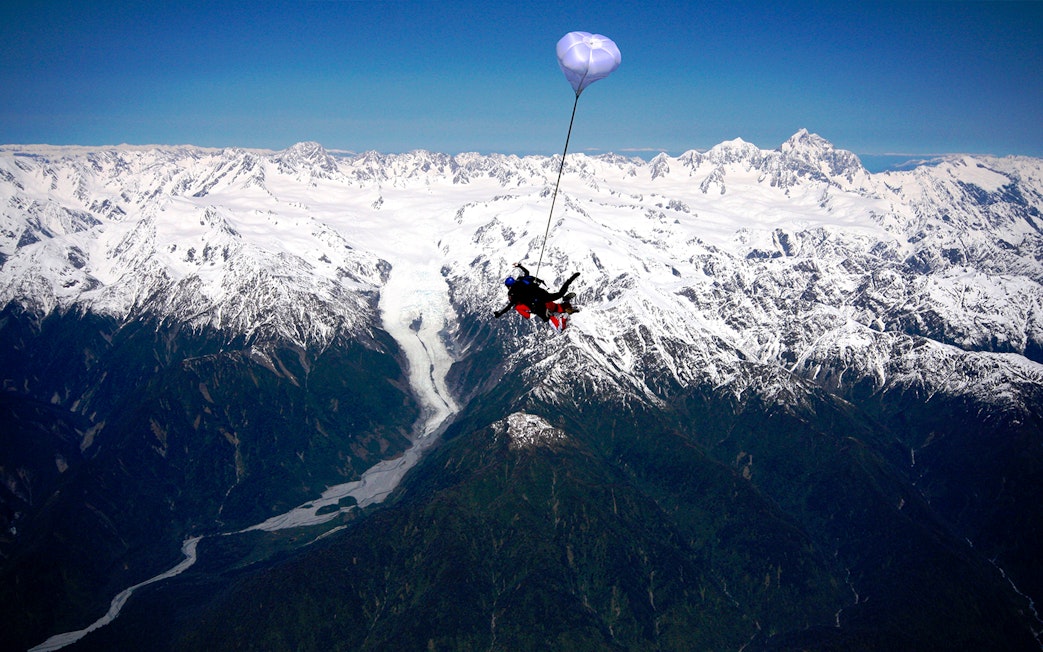 Skydiver over Franz Josef Glacier with snow-capped mountains in New Zealand.
