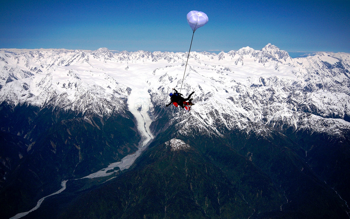 Skydiver over Franz Josef Glacier with snow-capped mountains in New Zealand.
