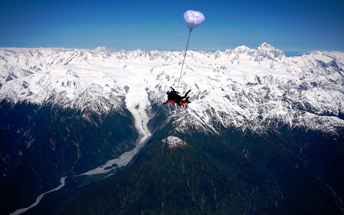 Skydiver over Franz Josef Glacier with snow-capped mountains in New Zealand.