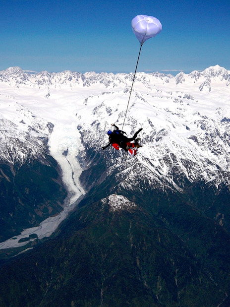 Skydiver over Franz Josef Glacier with snow-capped mountains in New Zealand.