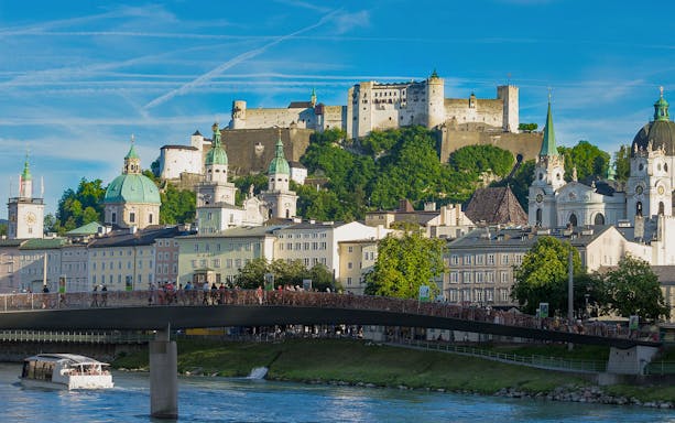 Fortress Hohensalzburg overlooking Salzburg with a river cruise boat in the foreground.