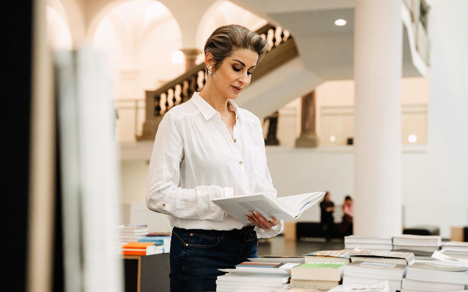 Woman browsing books in a museum shop with grand staircase in background.