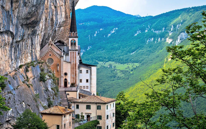 Madonna della Corona Sanctuary nestled in cliffs with lush green mountains in the background.