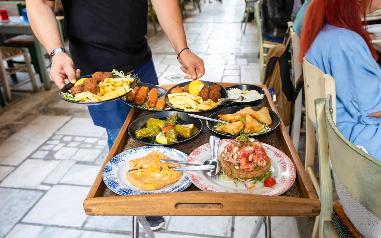 Traditional Greek dishes being served on a tray in a restaurant setting.