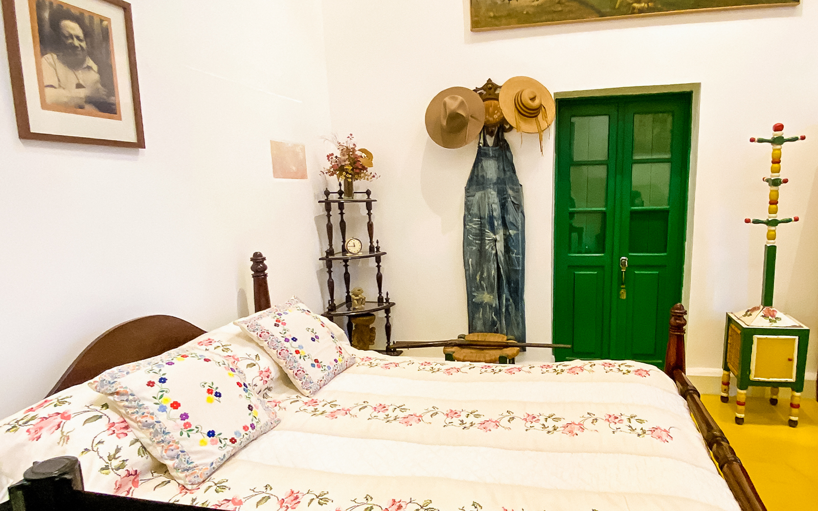 Frida Kahlo Museum bedroom with floral bedspread, green door, and hats on wall.