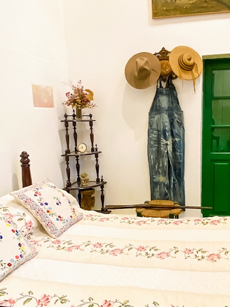 Frida Kahlo Museum bedroom with floral bedspread, green door, and hats on wall.