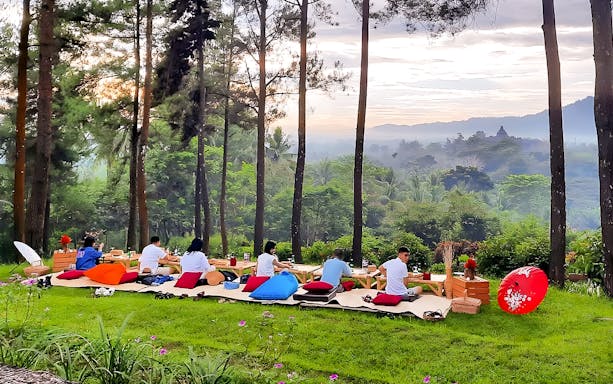 Tourists enjoying breakfast in a forest setting near Borobudur and Prambanan, Indonesia.