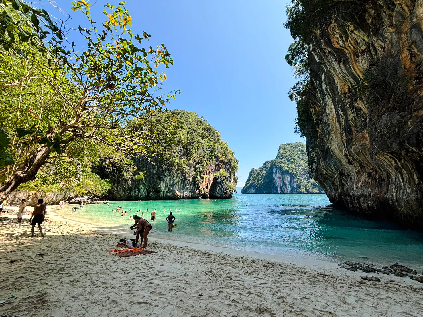 Tourists enjoying the beach and snorkeling at Hong Islands, Krabi, with limestone cliffs and clear water.