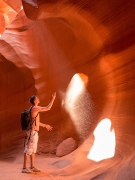 Young man with backpack exploring Antelope Canyon, Page, with sunlight streaming through.