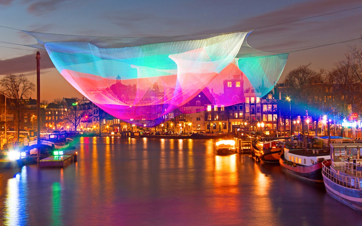 Colorful light installation over Amsterdam canal during Lights Festival.