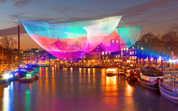 Colorful light installation over Amsterdam canal during Lights Festival.