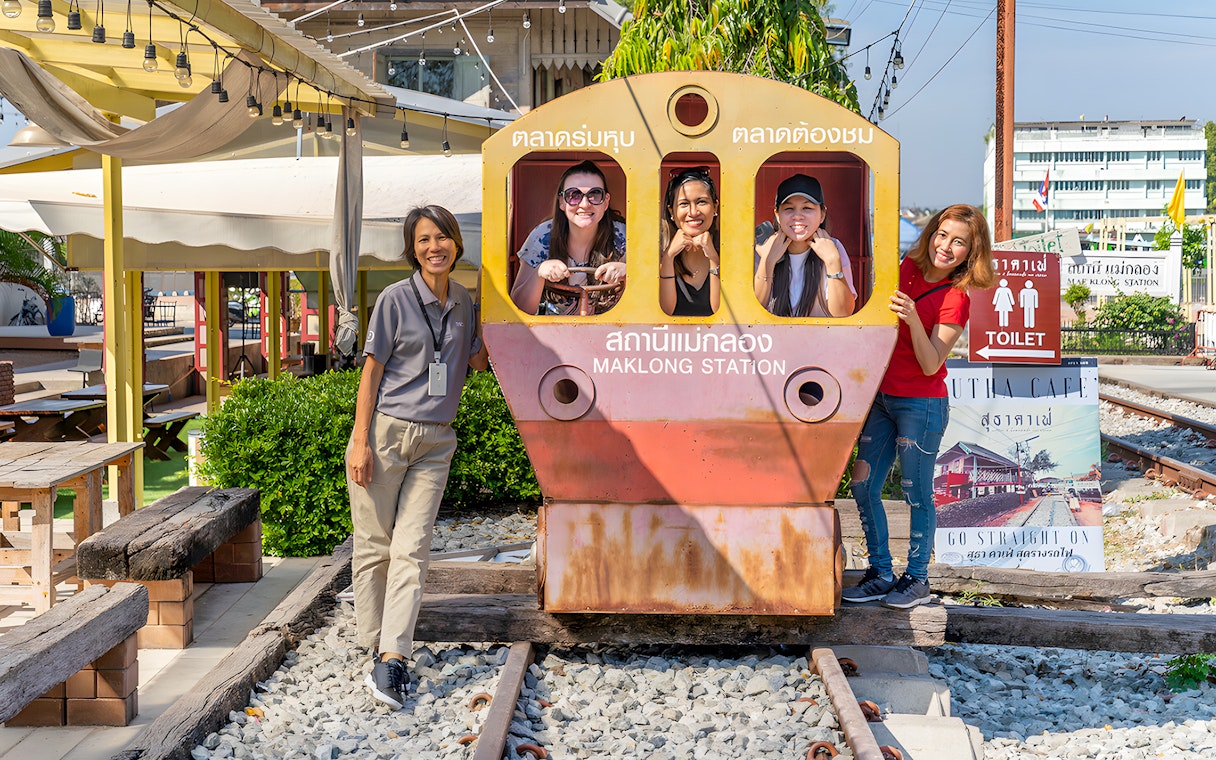 Visitors posing with a train cutout at Maeklong Railway Market station.