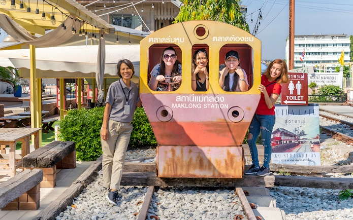 Visitors posing with a train cutout at Maeklong Railway Market station.
