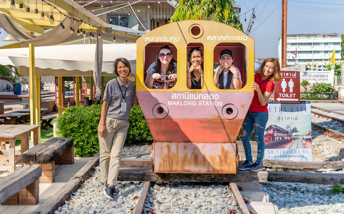 Visitors posing with a train cutout at Maeklong Railway Market station.