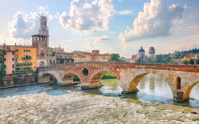 Ponte Pietra bridge over the Adige River in Verona, Italy, with historic buildings in the background.