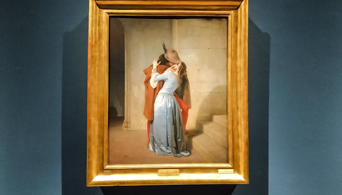 A romantic scene of a woman and man in an intimate embrace, painted by Hayez, located in Milan's Pinacoteca di Brera.