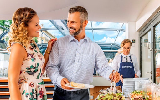 Couple enjoying buffet on Vltava River sightseeing cruise in Prague.