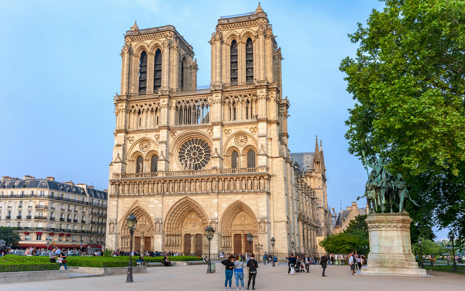 Die Fassade der Kathedrale Notre-Dame in Paris mit umliegenden Besuchern und einer Statue auf dem Vorplatz