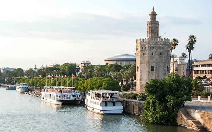 Torre del Oro by the Guadalquivir River in Seville, Spain, with tour boats docked nearby.
