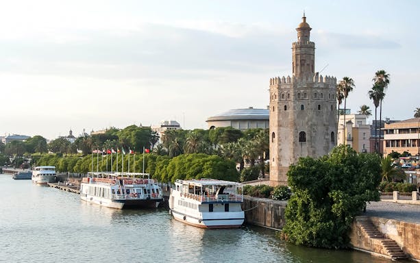 Torre del Oro by the Guadalquivir River in Seville, Spain, with tour boats docked nearby.
