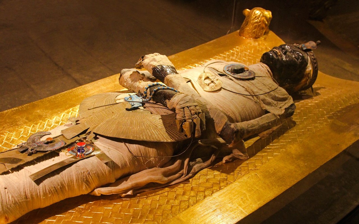 Mummy display at the Grand Egyptian Museum, featuring intricate ancient jewelry and golden sarcophagus.
