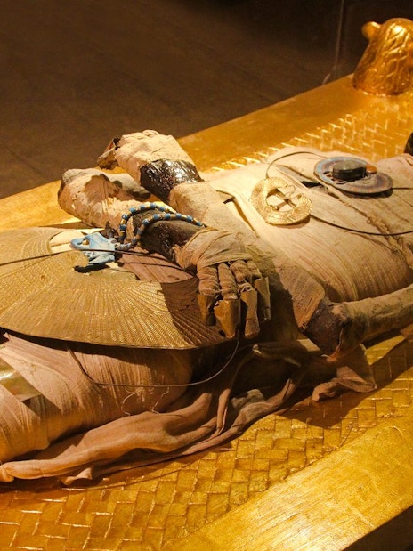 Mummy display at the Grand Egyptian Museum, featuring intricate ancient jewelry and golden sarcophagus.