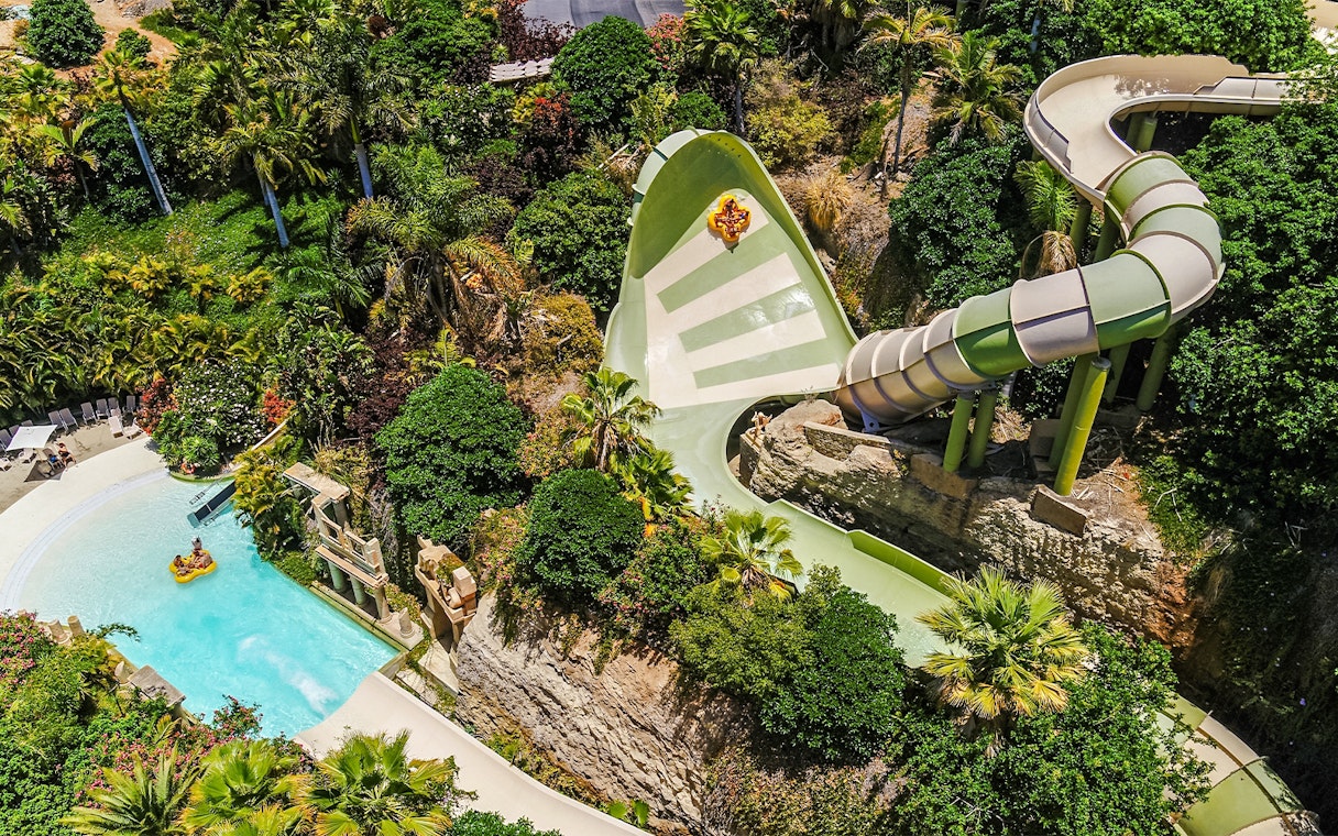 Tourists on Kinnaree ride at Siam Park, surrounded by lush greenery and water slide.