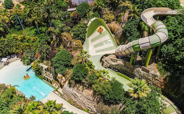 Tourists on Kinnaree ride at Siam Park, surrounded by lush greenery and water slide.
