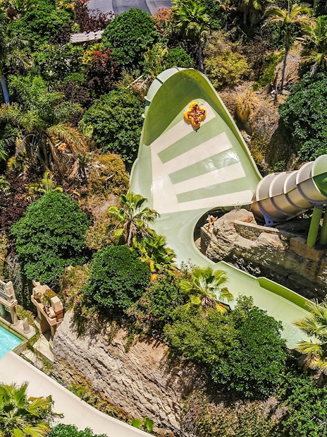 Tourists on Kinnaree ride at Siam Park, surrounded by lush greenery and water slide.