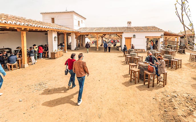 Visitors walking and dining in a rustic courtyard at Puy du Fou España Park.