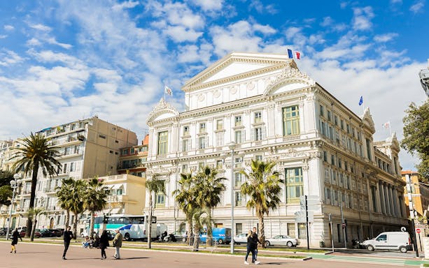 Nice Old Town building with palm trees and people walking nearby, France.