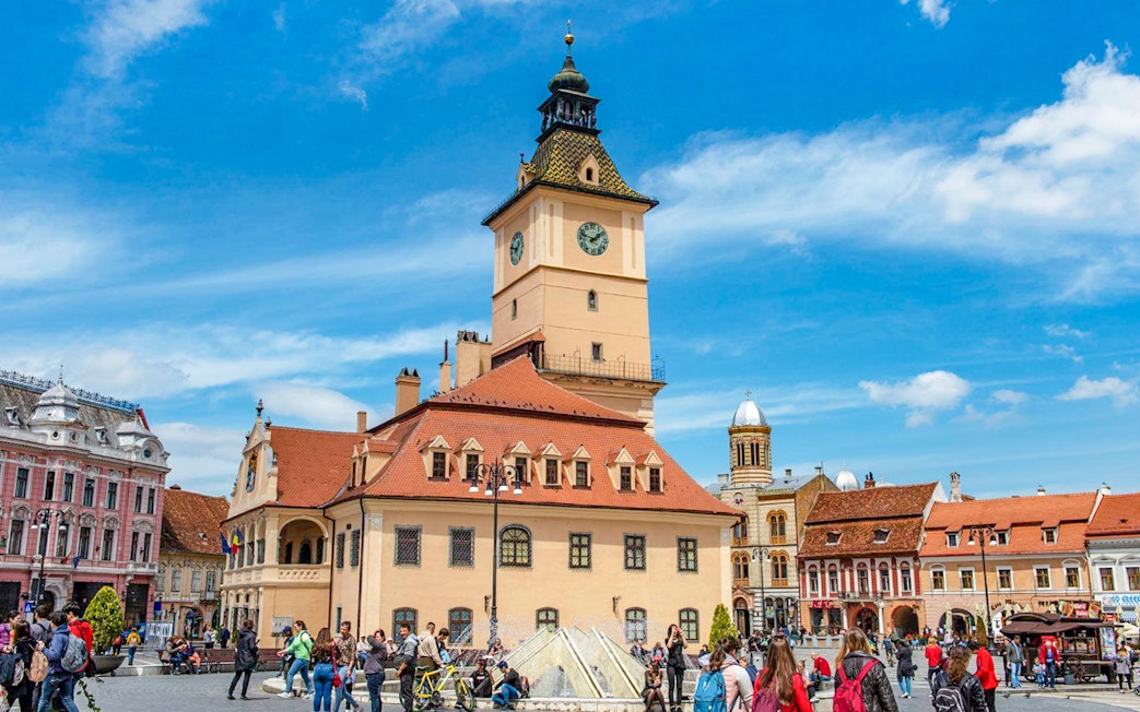 Medieval clock tower in Brașov's Council Square with tourists exploring.