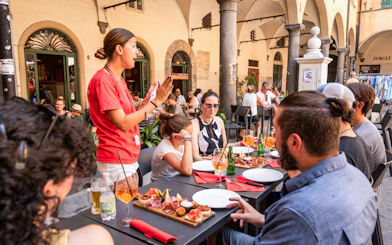 Tour guide speaking to visitors having lunch in Pisa outdoor cafe.