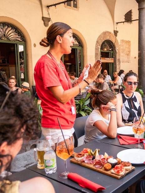 Tour guide speaking to visitors having lunch in Pisa outdoor cafe.