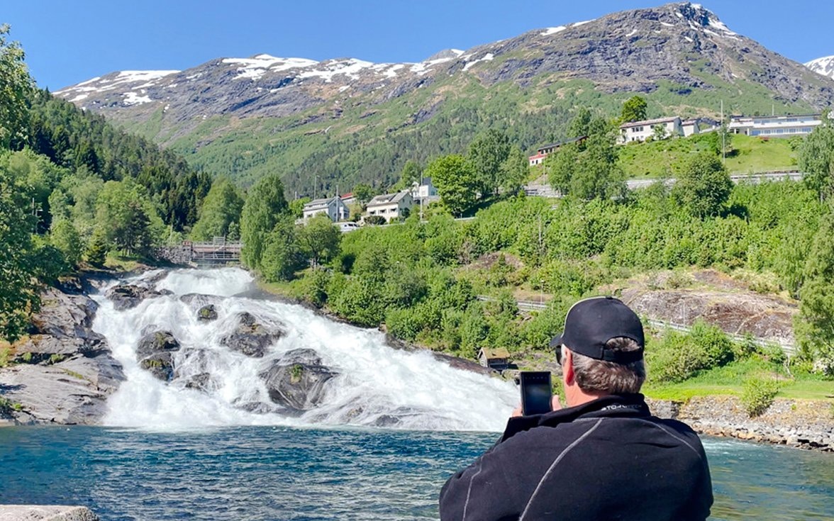 Man photographing Hellesylt waterfall from boat, Geiranger Fjord, Norway.