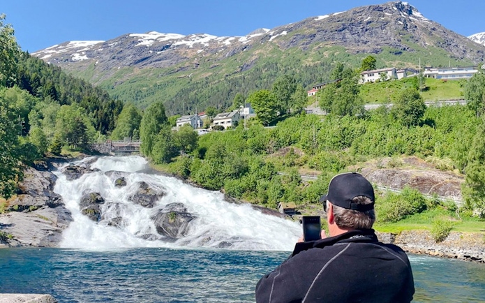 Man photographing Hellesylt waterfall from boat, Geiranger Fjord, Norway.