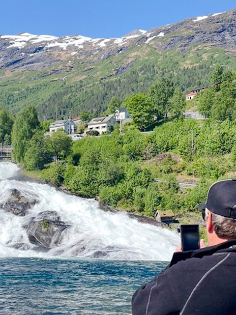 Man photographing Hellesylt waterfall from boat, Geiranger Fjord, Norway.