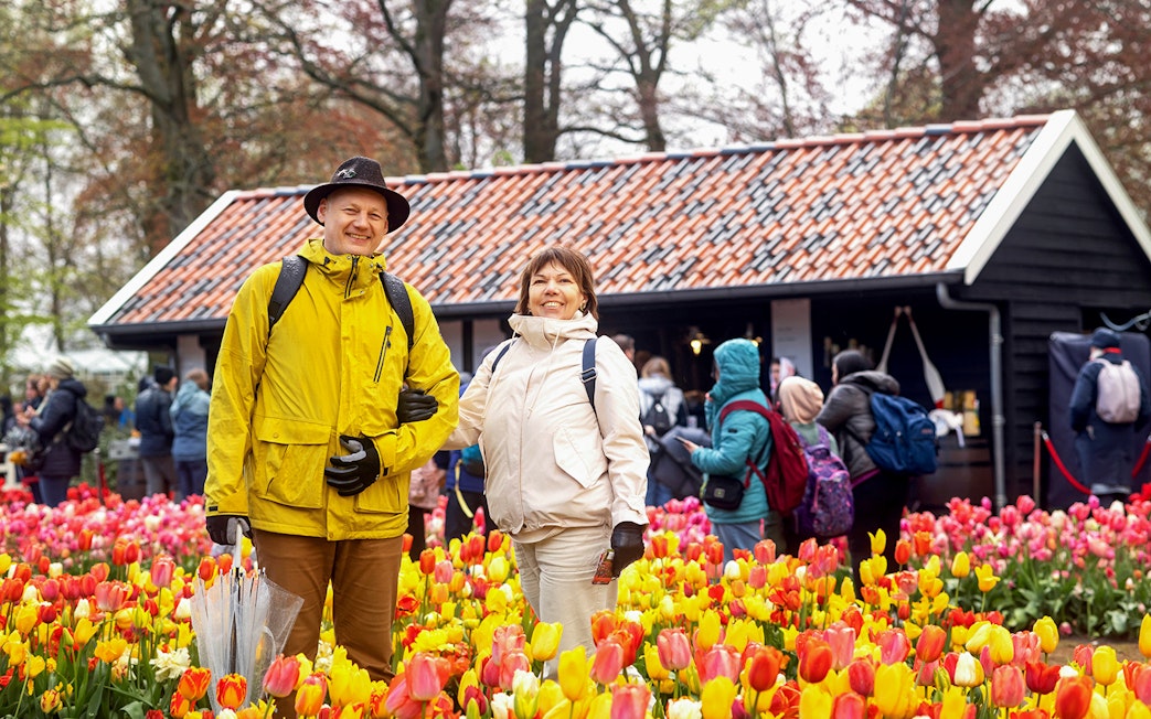 Visitors enjoying tulip fields at Keukenhof with a rustic building in the background.