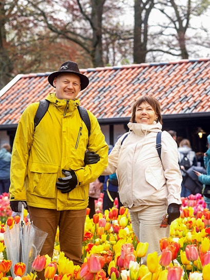 Visitors enjoying tulip fields at Keukenhof with a rustic building in the background.