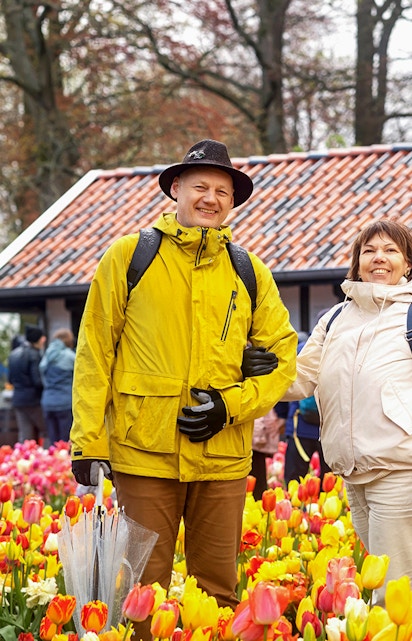 Visitors enjoying tulip fields at Keukenhof with a rustic building in the background.