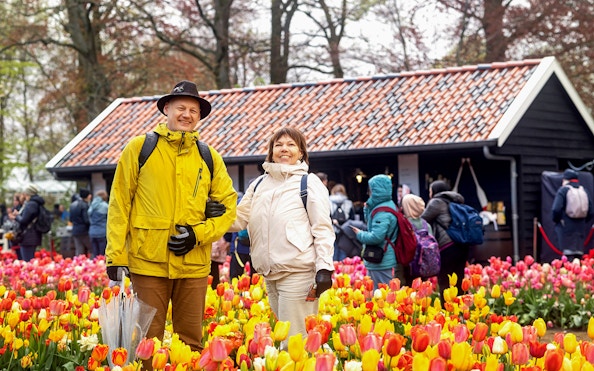 Visitors enjoying tulip fields at Keukenhof with a rustic building in the background.