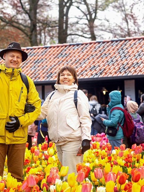 Visitors enjoying tulip fields at Keukenhof with a rustic building in the background.