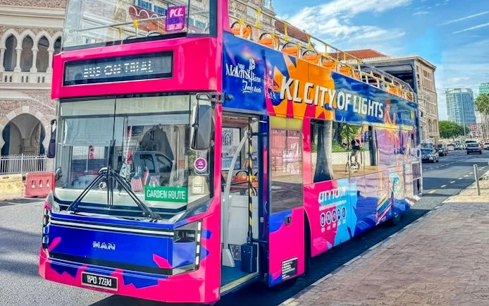 Colorful double-decker bus for Kuala Lumpur city tour parked near historical building.