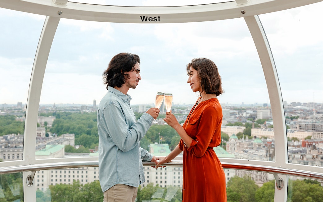 Couple toasting with champagne inside the London Eye capsule, overlooking cityscape.